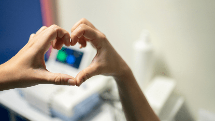 Image of an individual's hands gesturing the heart sign over an ultrasound machine.